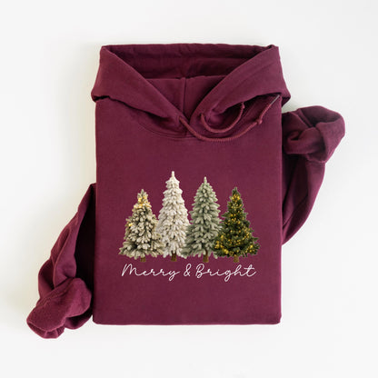 May include: A maroon hoodie featuring a festive design. The graphic includes four stylized Christmas trees in varying shades of green and white, with one tree adorned with yellow lights. The words "Merry & Bright" are written in a cursive font below the trees.