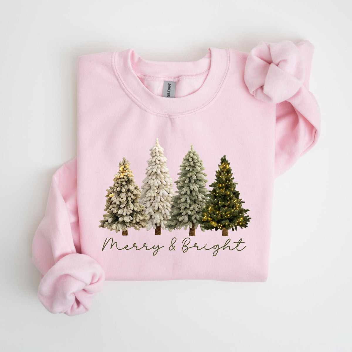 May include: A light pink sweatshirt featuring four Christmas trees with varying shades of green and white. The trees are decorated with lights. The words "Merry & Bright" are written in a cursive font below the trees.