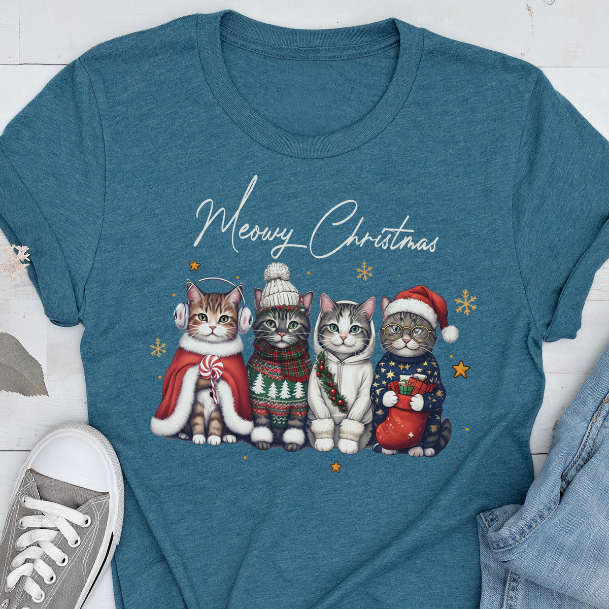 May include: A teal crew neck t-shirt featuring a graphic of four cats wearing winter accessories and the text Meowy Christmas. The cats are dressed in a red cape with earmuffs, a knit hat and sweater, a white hoodie with a wreath, and a Santa hat.