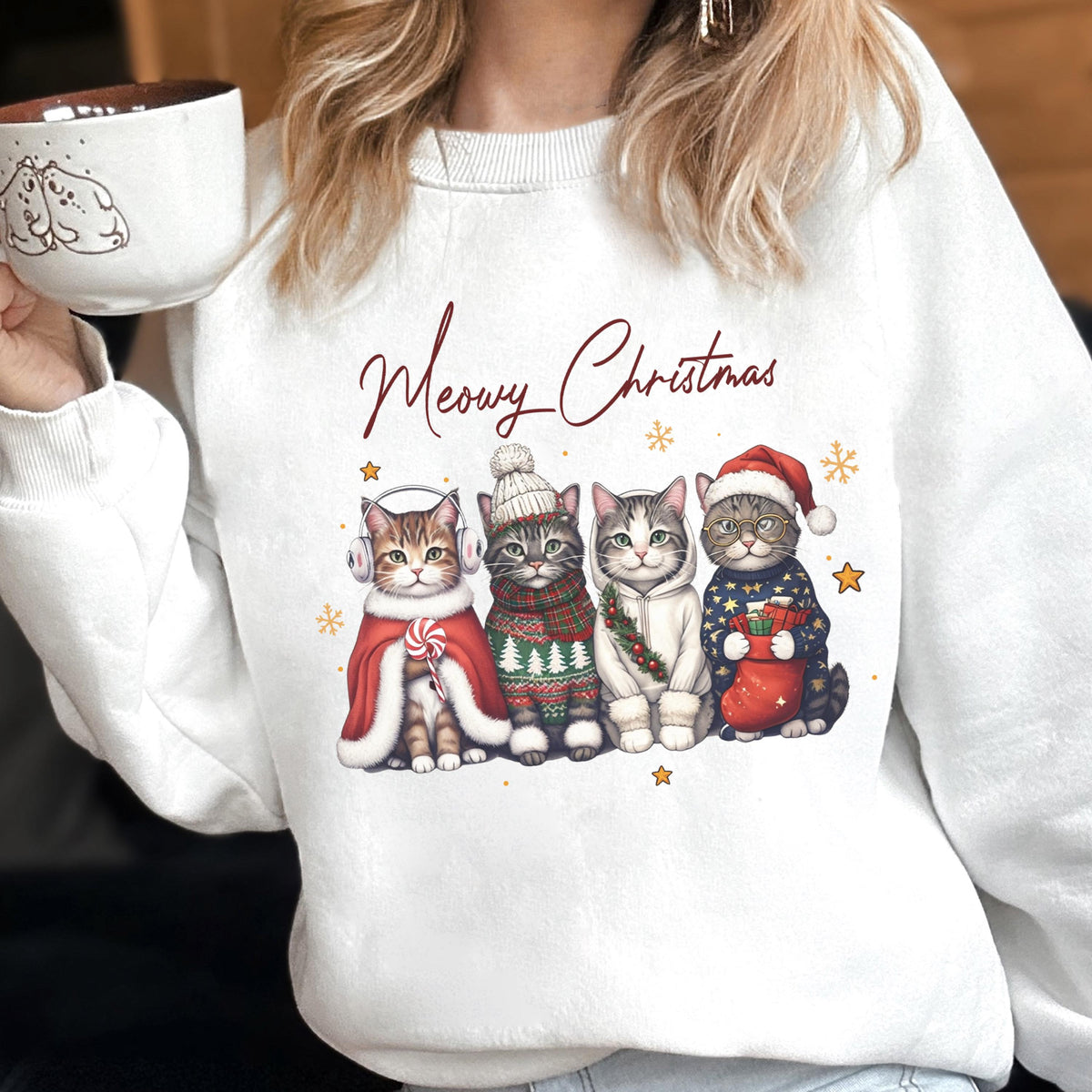 May include: A white crewneck sweatshirt featuring a graphic of four cats wearing winter accessories and the text Meowy Christmas. The cats are dressed in a red cape with earmuffs, a knit hat and scarf, a white hoodie, and a Santa hat with a sweater.