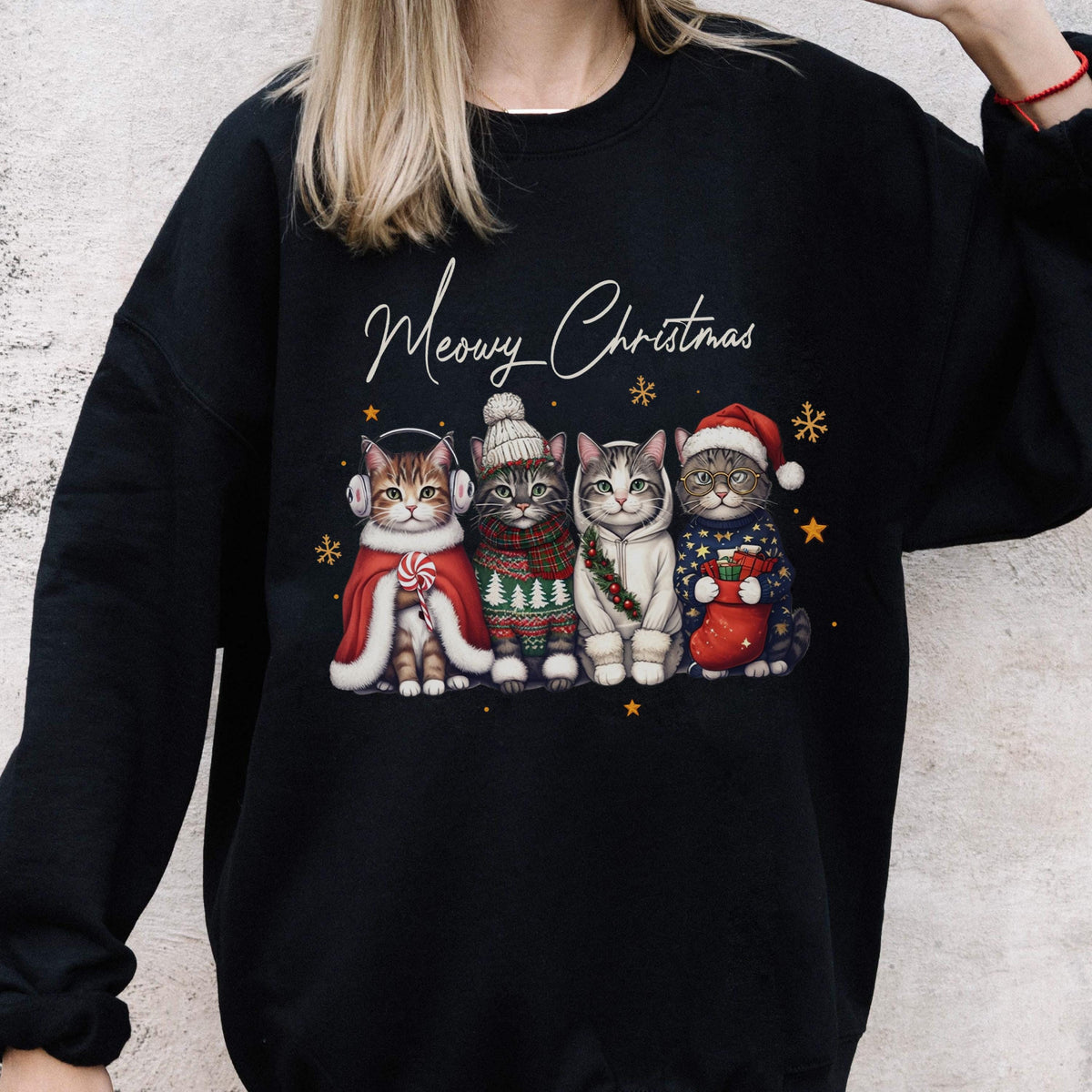 May include: A black long-sleeve sweatshirt featuring a graphic of four cats wearing winter accessories and the text Meowy Christmas. The cats are dressed in a red cape, a knit sweater, a white hoodie, and a blue sweater with a red stocking.