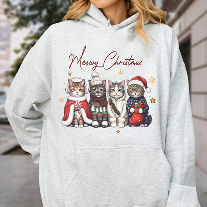 May include: A light gray hooded sweatshirt featuring a graphic of four cats wearing winter accessories and the text Meowy Christmas. The cats are adorned with earmuffs, a knit hat, a scarf, and a Santa hat, surrounded by small gold stars.