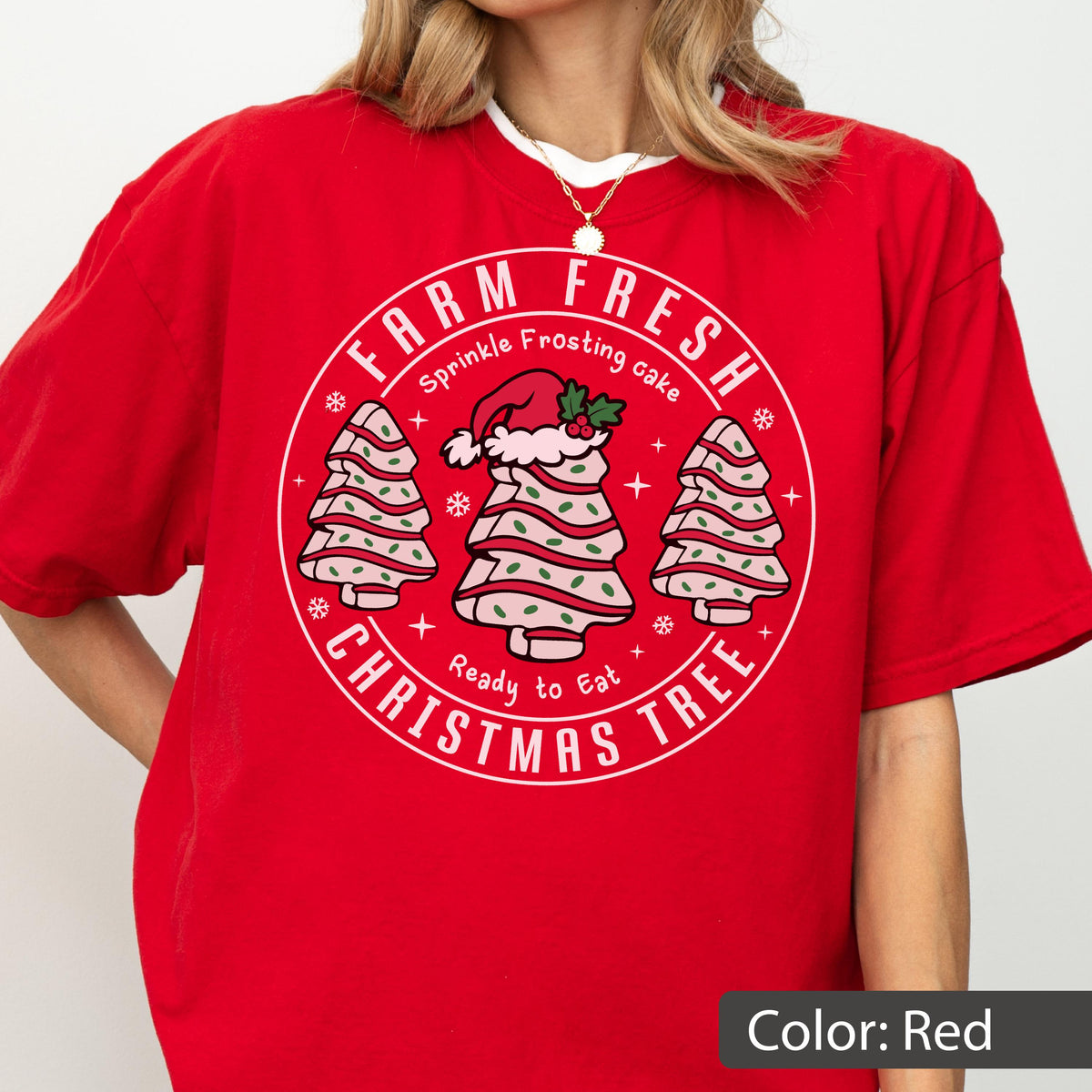 May include: A red short-sleeved t-shirt featuring a circular graphic with the text "FARM FRESH CHRISTMAS TREE" and "Sprinkle Frosting cake Ready to Eat". The design includes three stylized cake trees with pink frosting, green sprinkles, and a Santa hat.