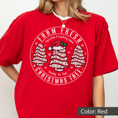 May include: A red short-sleeved t-shirt featuring a circular graphic with the text "FARM FRESH CHRISTMAS TREE" and "Sprinkle Frosting cake Ready to Eat". The design includes three stylized cake trees with pink frosting, green sprinkles, and a Santa hat.