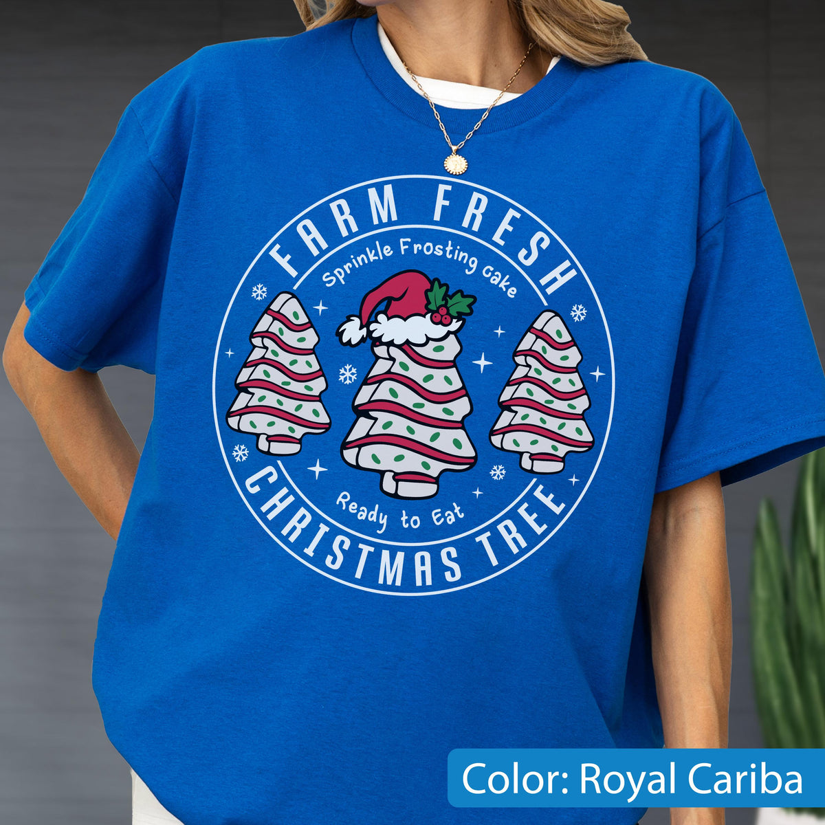 May include: A royal blue t-shirt featuring a circular graphic with the text "FARM FRESH CHRISTMAS TREE" and "Sprinkle Frosting cake Ready to Eat". The design includes three white tree-shaped cakes with red stripes, green sprinkles, and a Santa hat.