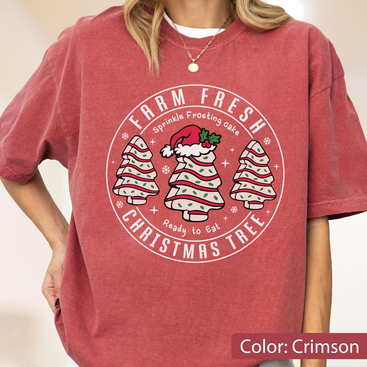May include: A crimson short-sleeve t-shirt featuring a circular graphic with the text FARM FRESH CHRISTMAS TREE, Sprinkle Frosting cake, and Ready to Eat. The design includes three stylized Christmas trees with white frosting and green sprinkles.