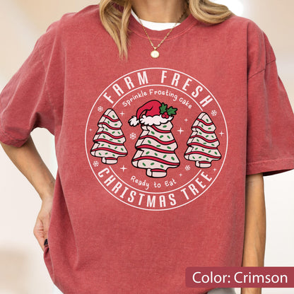 May include: A crimson short-sleeve t-shirt featuring a circular graphic with the text FARM FRESH CHRISTMAS TREE, Sprinkle Frosting cake, and Ready to Eat. The design includes three stylized Christmas trees with white frosting and green sprinkles.