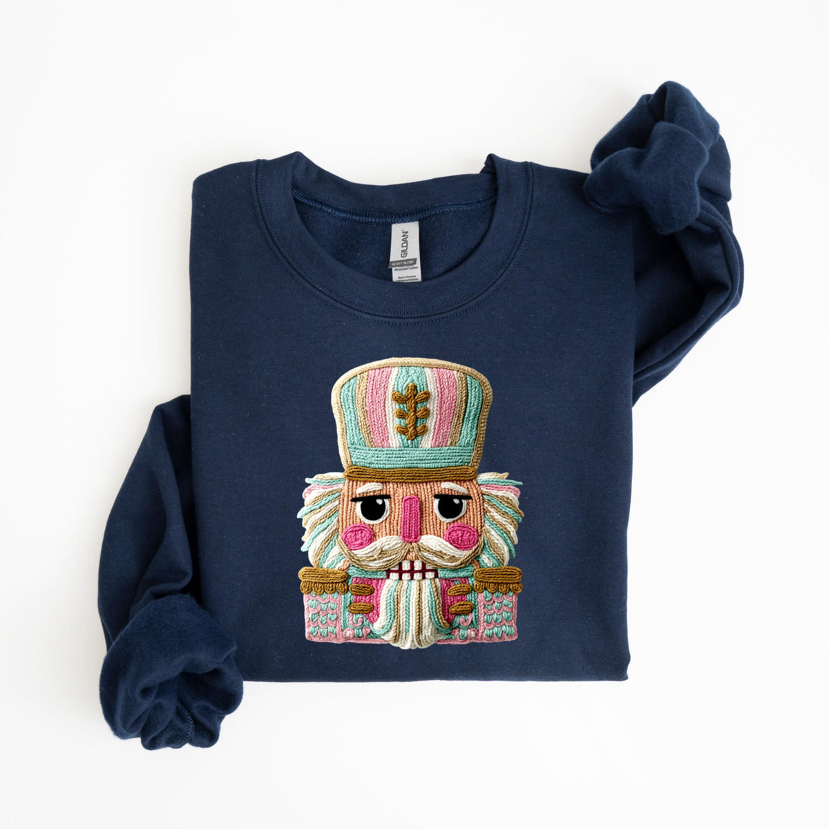 May include: Navy blue sweatshirt featuring a colorful embroidered nutcracker design. The nutcracker has a pink face, a white mustache, and a tall hat with pink, blue, and green stripes. The design is centered on the front of the sweatshirt.