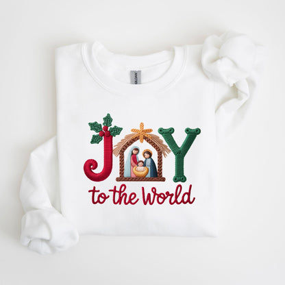 May include: White sweatshirt with an embroidered design. The design features the word "JOY" in red, green, and gold, with a nativity scene in the center. The phrase "to the world" is embroidered in red below the word "JOY".
