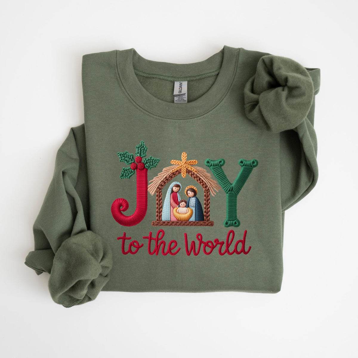 May include: Olive green sweatshirt with embroidered text and design. The design features the word "JOY" with a nativity scene and the phrase "to the world" in red. The sweatshirt has long sleeves and a crew neck.