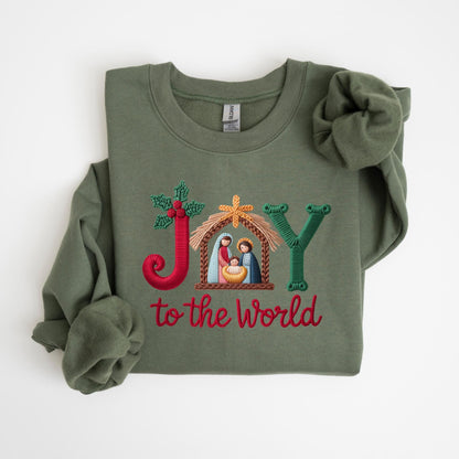 May include: Olive green sweatshirt with embroidered text and design. The design features the word "JOY" with a nativity scene and the phrase "to the world" in red. The sweatshirt has long sleeves and a crew neck.