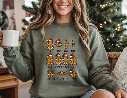 May include: An olive green sweatshirt featuring a graphic of gingerbread men wearing Santa hats, illustrating fractions. The fractions include 1, 1/2, 1/4, and 1/8. The sweatshirt is a festive and educational design.