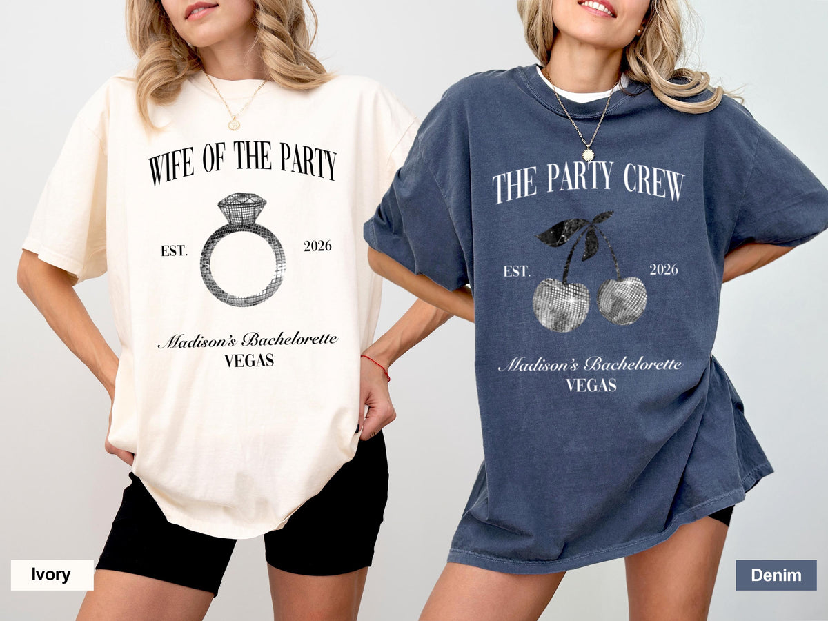 May include: Two oversized t-shirts, one ivory and one denim blue, feature text and graphics. The ivory shirt says "Wife of the Party" with a ring graphic. The denim shirt says "The Party Crew" with a cherry graphic. Both shirts include "Madison's Bachelorette VEGAS".