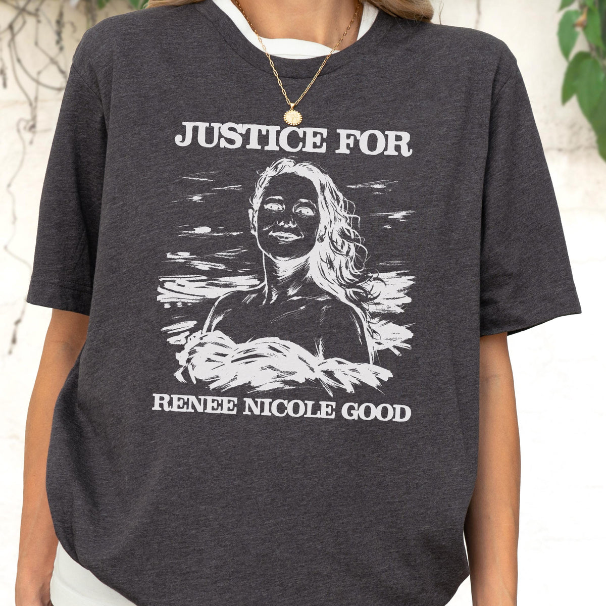 May include: Dark gray t-shirt with a white graphic of a woman and the text "JUSTICE FOR RENEE NICOLE GOOD". The shirt has a crew neck and short sleeves.
