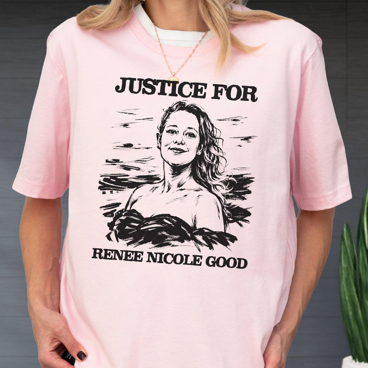 May include: A light pink t-shirt featuring the text "JUSTICE FOR" above a black and white portrait of a woman. Below the portrait, the text reads "RENEE NICOLE GOOD". The shirt has short sleeves and a crew neck.