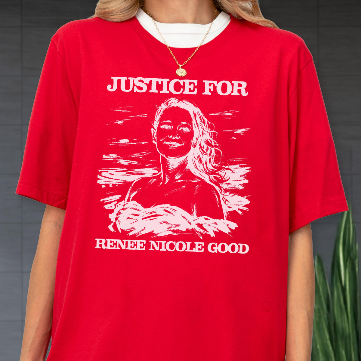 May include: Red t-shirt with the text "JUSTICE FOR" above a white illustration of a woman with long hair, and the text "RENEE NICOLE GOOD" below. The shirt has a white collar and is worn with a gold necklace.