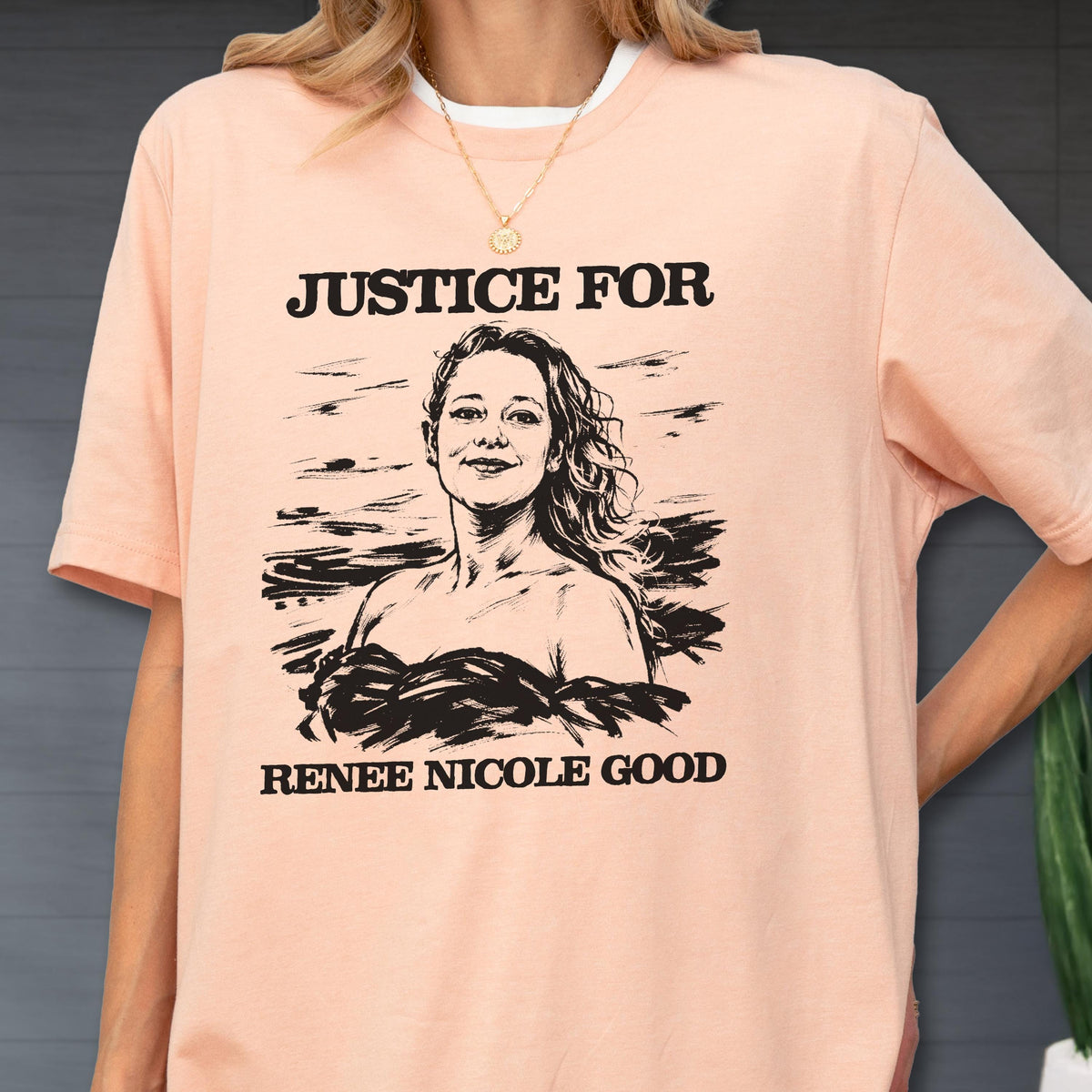 May include: Peach-colored t-shirt with the text "JUSTICE FOR" above a black and white illustration of a woman. Below the illustration is the text "RENEE NICOLE GOOD". The shirt has a white collar.