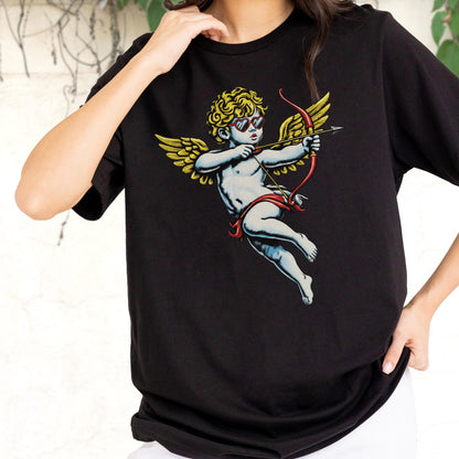 May include: A black short-sleeve t-shirt featuring a graphic print of a cherub with curly blonde hair, wearing heart-shaped sunglasses, and holding a red bow and arrow. The cherub has large golden wings and is positioned in the center of the shirt.