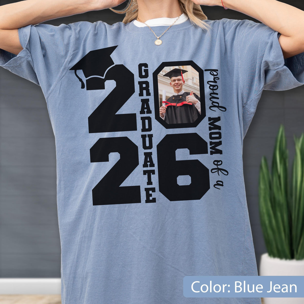 May include: Blue jean colored t-shirt with a large black graphic that reads "2026 Graduate". The number "26" has a photo of a graduate in a cap and gown. The text "proud MOM of a" is printed on the right side.
