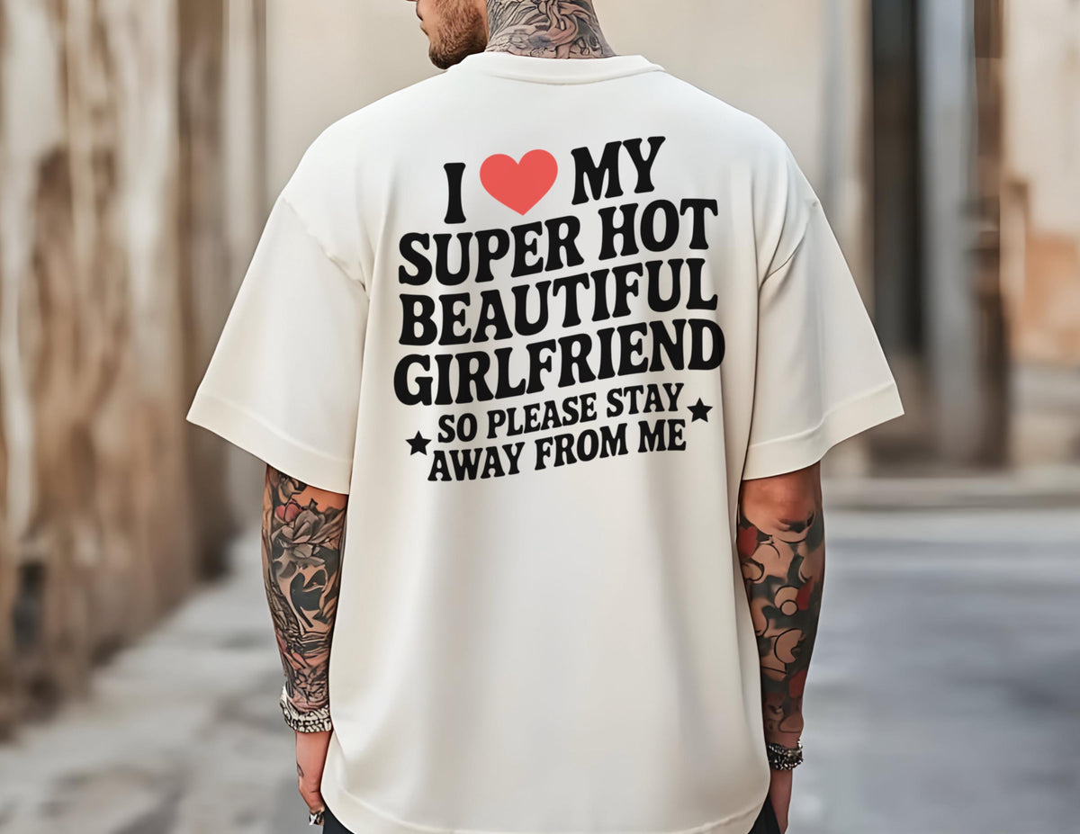 May include: Cream-colored t-shirt with the text "I ❤️ MY SUPER HOT BEAUTIFUL GIRLFRIEND SO PLEASE STAY AWAY FROM ME" in black and red. The shirt has short sleeves and a relaxed fit.