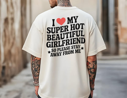 May include: Cream-colored t-shirt with the text "I ❤️ MY SUPER HOT BEAUTIFUL GIRLFRIEND SO PLEASE STAY AWAY FROM ME" in black and red. The shirt has short sleeves and a relaxed fit.