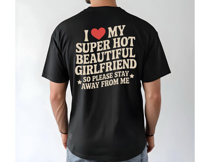 May include: Black t-shirt with the text "I ❤️ MY SUPER HOT BEAUTIFUL GIRLFRIEND SO PLEASE STAY AWAY FROM ME" in cream-colored letters and a red heart. The shirt is a short-sleeved crew neck.