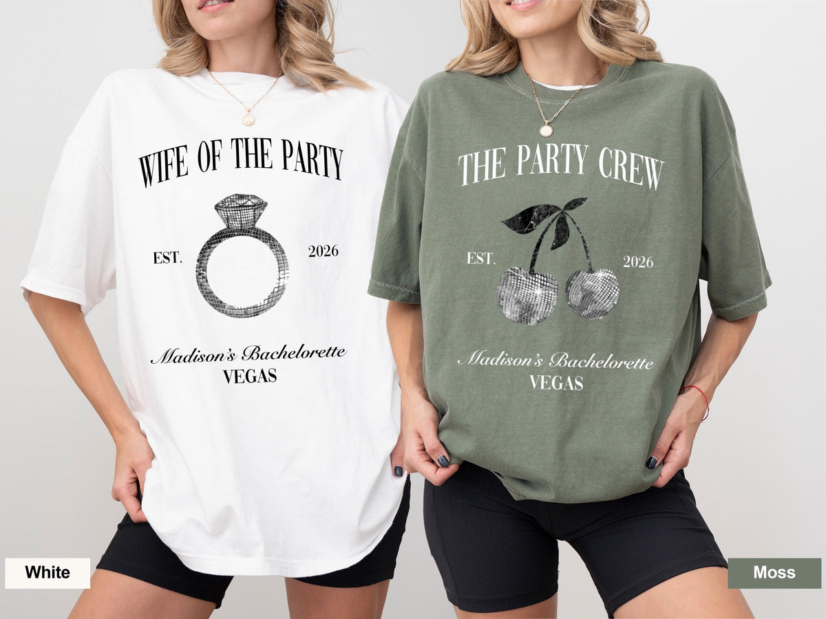 May include: Two t-shirts, one white and one moss green, with text and graphics. The white shirt says "WIFE OF THE PARTY" with a ring graphic. The green shirt says "THE PARTY CREW" with a cherry graphic. Both shirts have "Madison's Bachelorette VEGAS" and "2026".