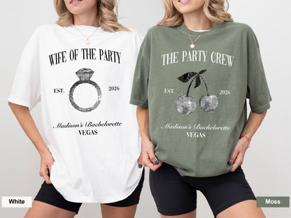 May include: Two t-shirts, one white and one moss green, with text and graphics. The white shirt says "WIFE OF THE PARTY" with a ring graphic. The green shirt says "THE PARTY CREW" with a cherry graphic. Both shirts have "Madison's Bachelorette VEGAS" and "2026".