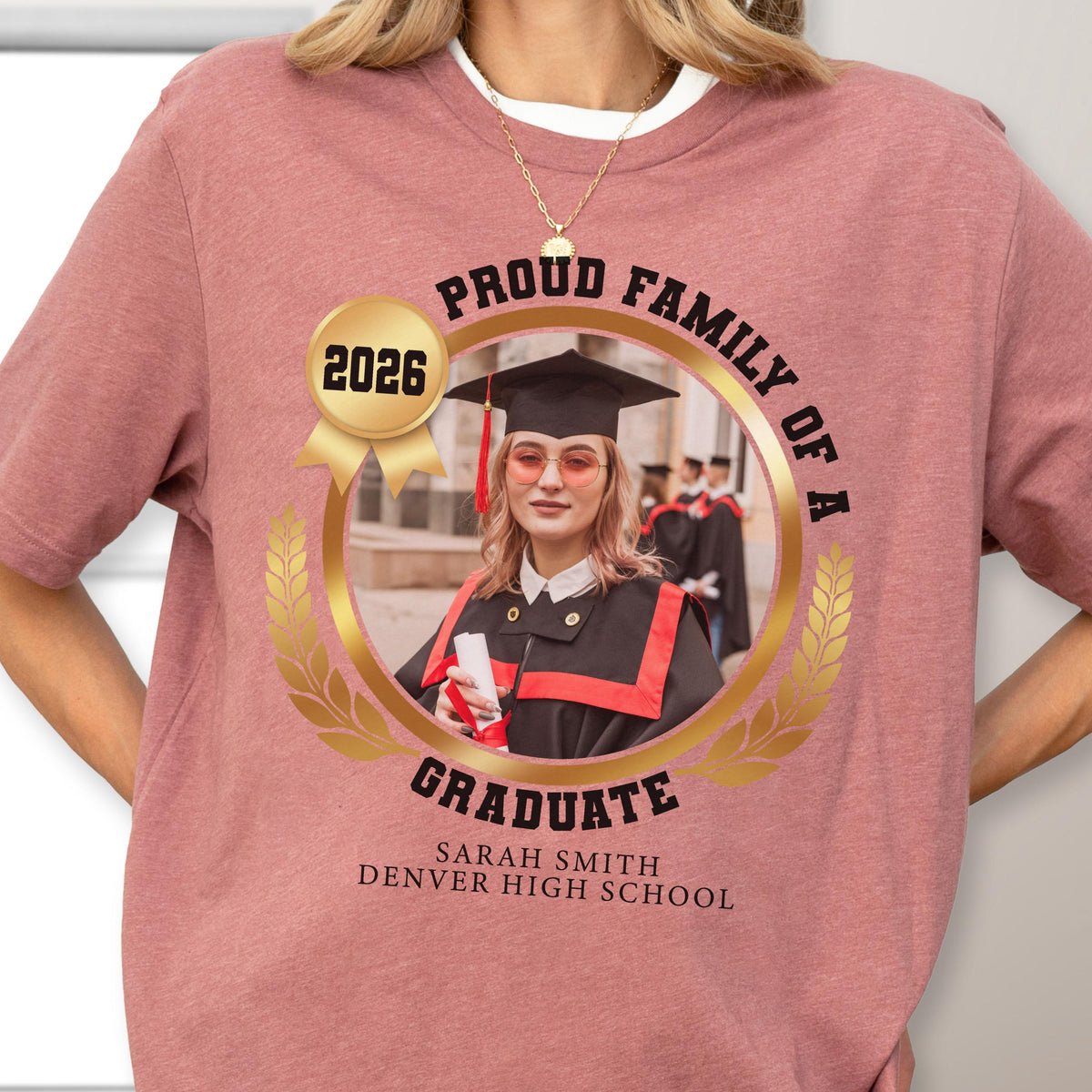 May include: A mauve t-shirt featuring a graduation photo design. The design includes the text "PROUD FAMILY OF A GRADUATE" around a photo of a graduate in a cap and gown, with the year "2026" and the graduate's name and school.