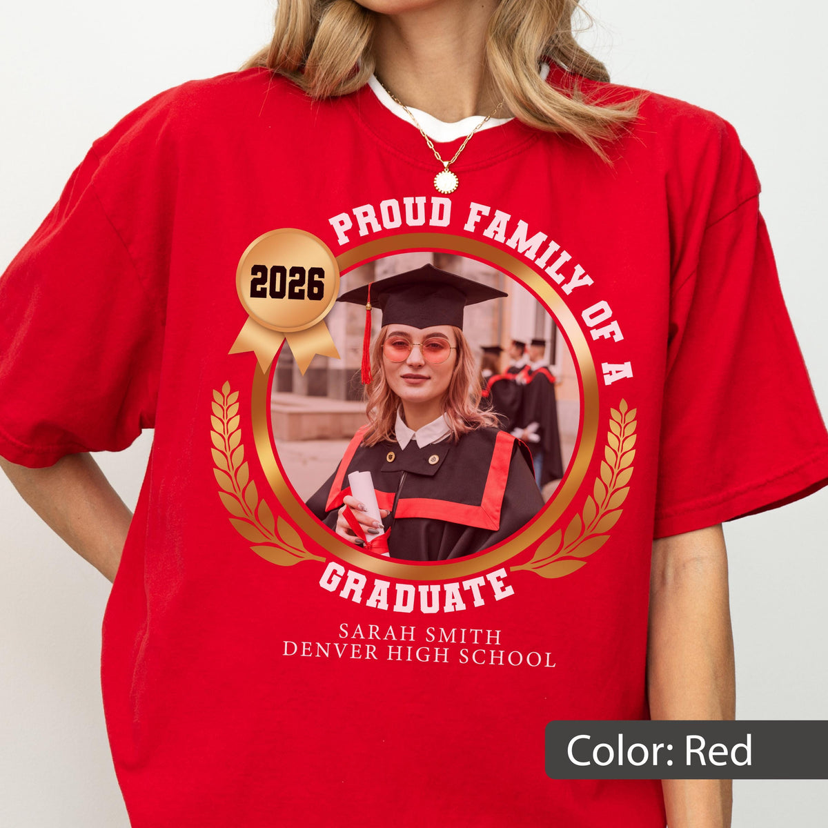 May include: Red t-shirt with a circular graphic featuring a graduate in a cap and gown, the text "PROUD FAMILY OF A GRADUATE", the year "2026", and the graduate's name and high school. The graphic is surrounded by a gold laurel wreath.