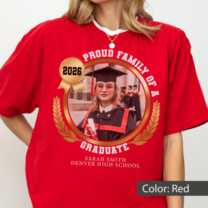May include: Red t-shirt with a circular graphic featuring a graduate in a cap and gown, the text "PROUD FAMILY OF A GRADUATE", the year "2026", and the graduate's name and high school. The graphic is surrounded by a gold laurel wreath.