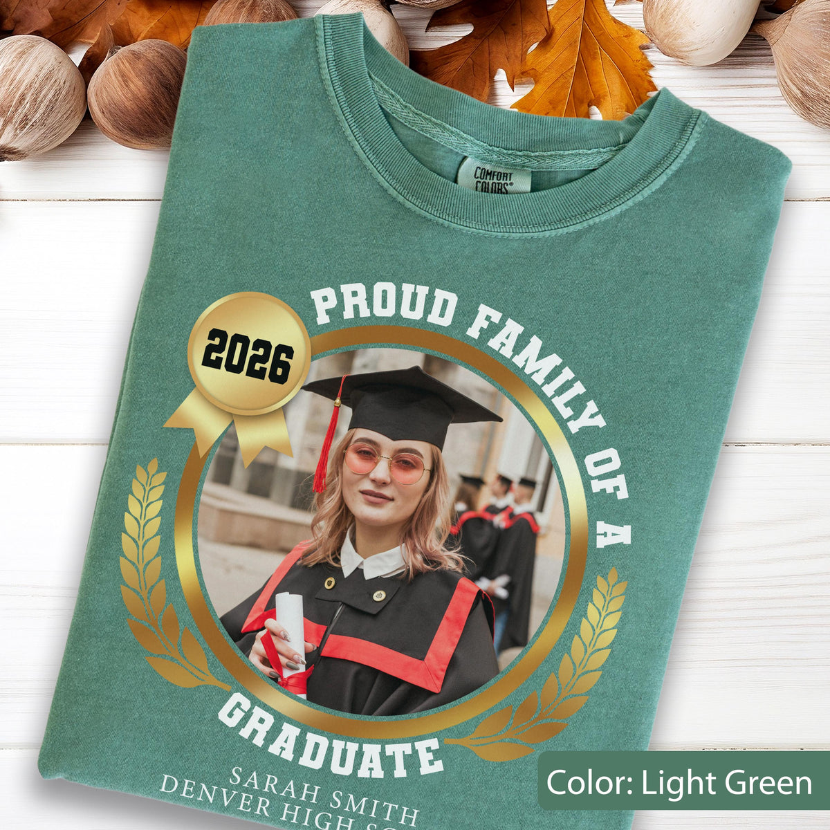 May include: Light green t-shirt with a graduation theme. The shirt features a gold emblem with the text "PROUD FAMILY OF A GRADUATE" and a photo of a graduate. The year "2026" is also displayed.