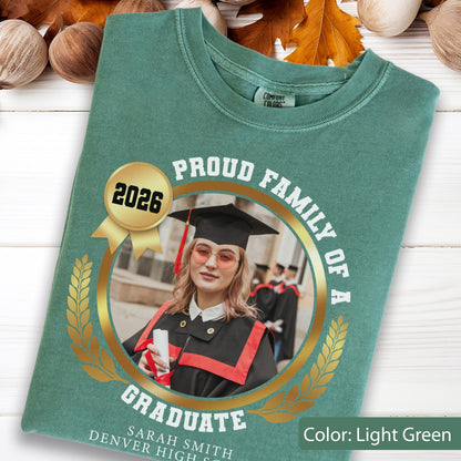 May include: Light green t-shirt with a graduation theme. The shirt features a gold emblem with the text "PROUD FAMILY OF A GRADUATE" and a photo of a graduate. The year "2026" is also displayed.
