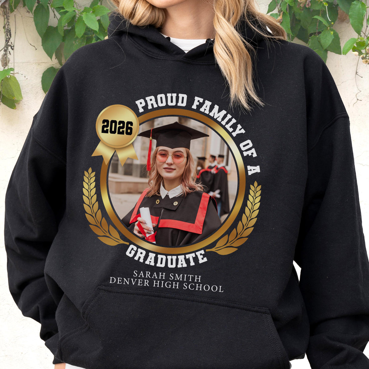 May include: Black hooded sweatshirt with a gold laurel wreath design. The design includes a photo of a graduate, the text "PROUD FAMILY OF A GRADUATE", the year "2026", and the graduate's name and high school.