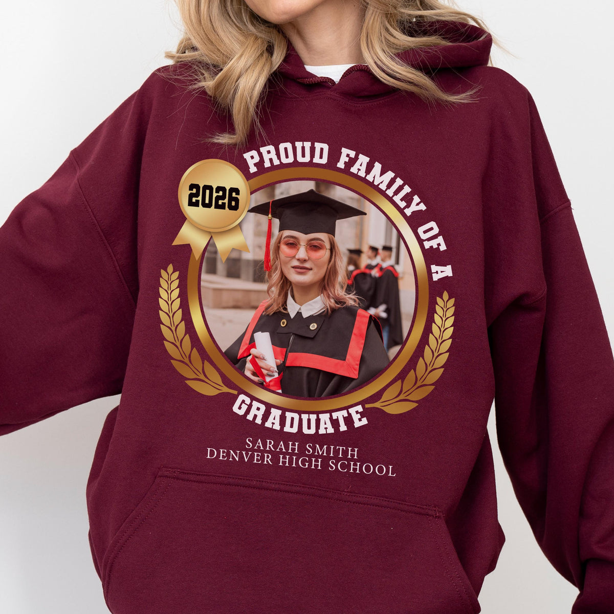 May include: Burgundy hoodie with a graduation photo in a gold frame. The photo features a graduate in a cap and gown. Text includes "Proud Family of a Graduate," the year "2026," and the graduate's name and high school.