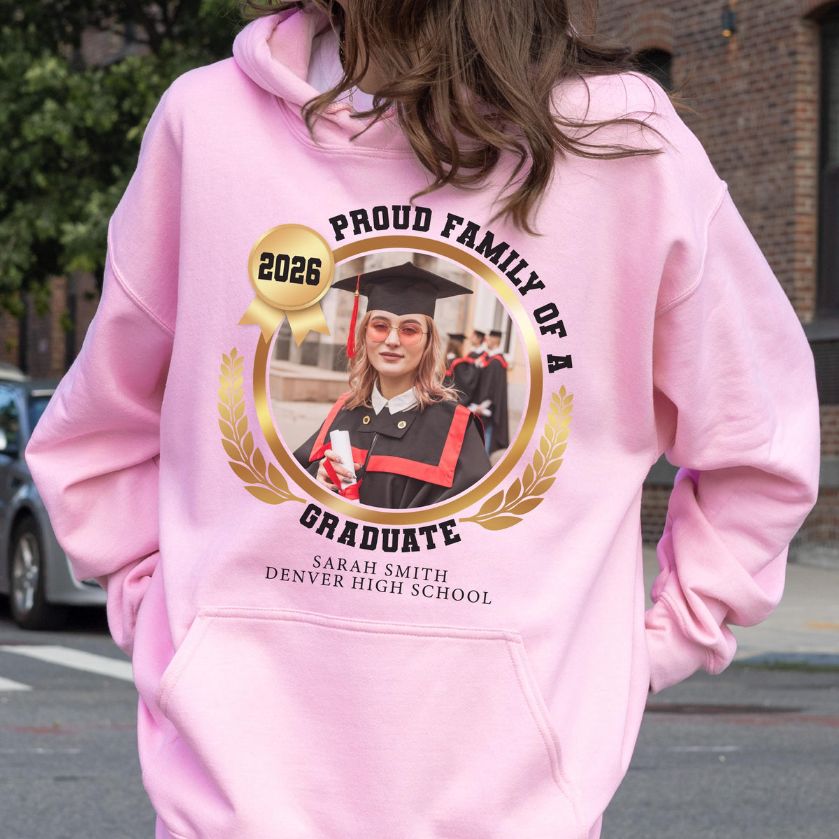 May include: Pink hooded sweatshirt with a graduation design. The design includes a photo of a graduate, the words "Proud Family of a Graduate", the year 2026, and the graduate's name and high school.