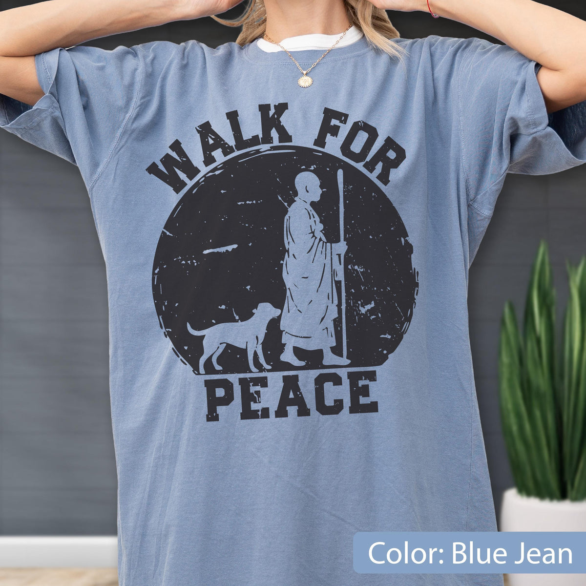 May include: Blue jean colored t-shirt with a distressed black graphic. The graphic features a figure with a dog and the words "WALK FOR PEACE". The shirt has short sleeves and a relaxed fit.