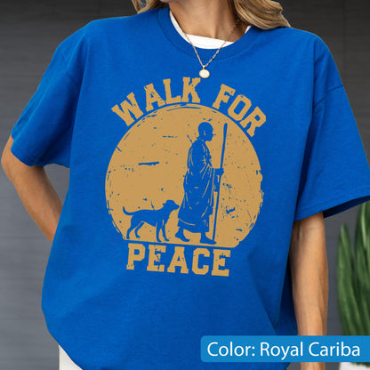 May include: Royal Cariba blue t-shirt with a round, distressed gold graphic. The graphic features a figure with a staff, a dog, and the words "WALK FOR PEACE". The shirt has short sleeves and a crew neck.