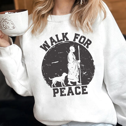 May include: White sweatshirt with a black graphic that reads "WALK FOR PEACE." The graphic features a person with a staff and a dog. A white mug with a dog illustration is held in the person's hand.