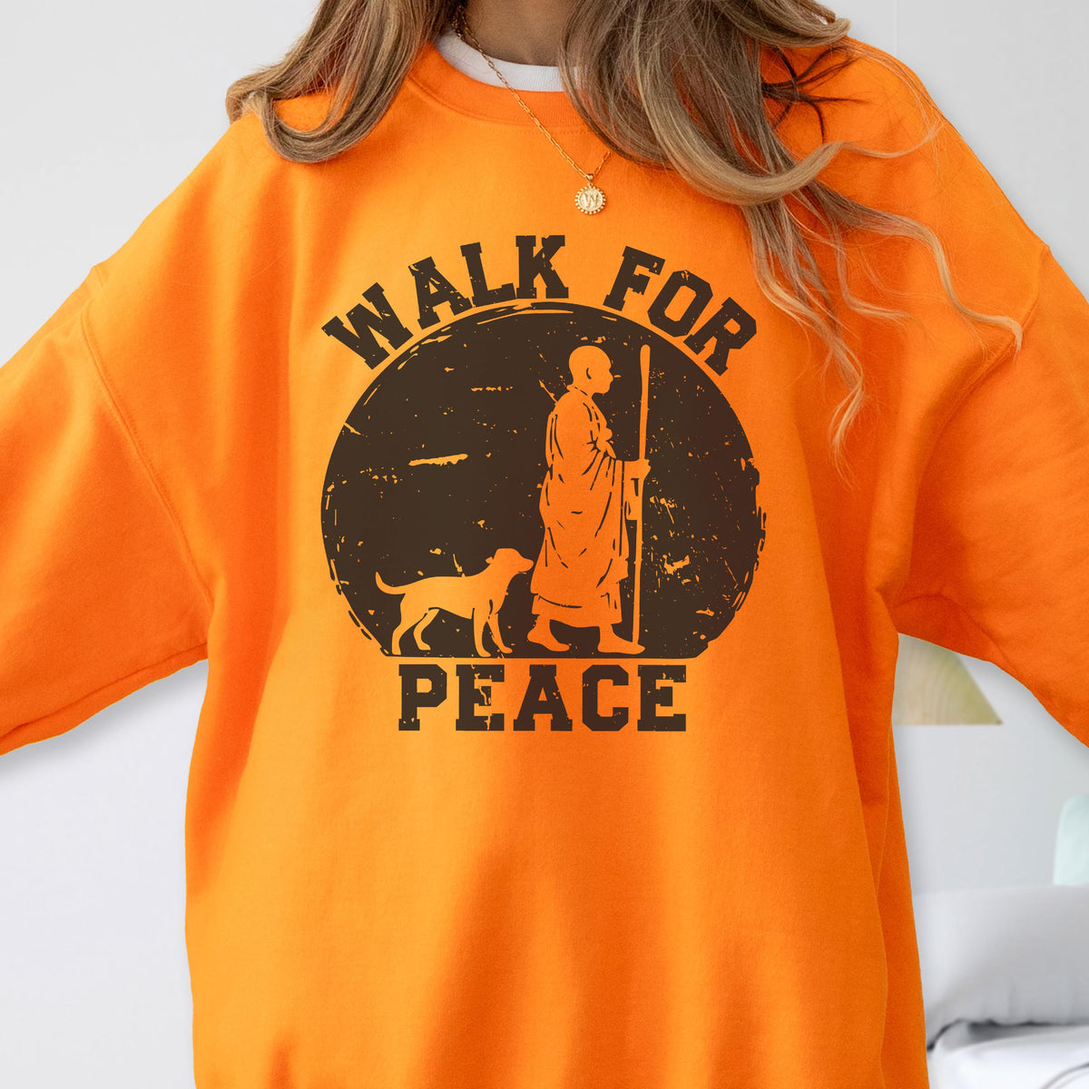 May include: Orange sweatshirt with a circular graphic featuring a figure with a staff, a dog, and the words "WALK FOR PEACE". The graphic is in shades of brown and black. The sweatshirt is a solid orange color.