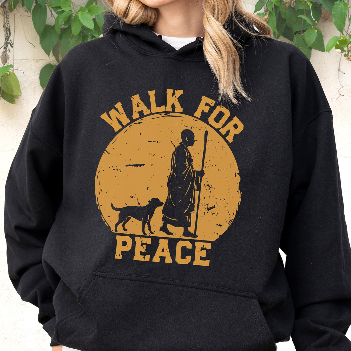 May include: Black hoodie with a graphic design featuring a person with a dog, walking with a staff, inside a gold circle. The words "WALK FOR PEACE" are printed in gold above and below the image.