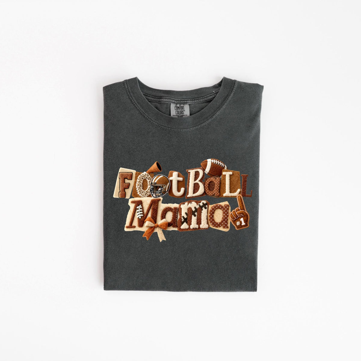 May include: Dark grey t-shirt with the words "Football Mama" in a decorative, layered design. The design includes footballs, a helmet, a bow, and a foam finger. The shirt is folded neatly on a white surface.