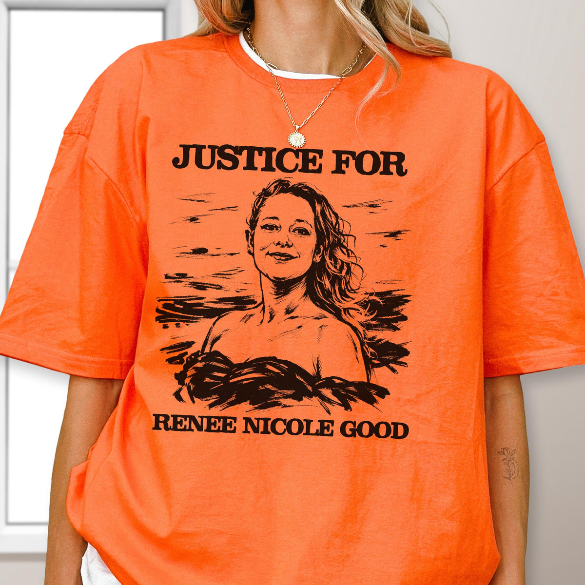 May include: Bright orange t-shirt with the text "JUSTICE FOR" above a black and white portrait of a woman. Below the portrait, the text reads "RENEE NICOLE GOOD". The shirt has short sleeves and a crew neck.