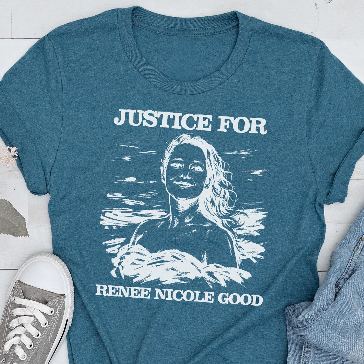May include: Teal t-shirt with the text "JUSTICE FOR" above a white illustration of a woman and the text "RENEE NICOLE GOOD" below. A gray sneaker is visible in the lower left corner.