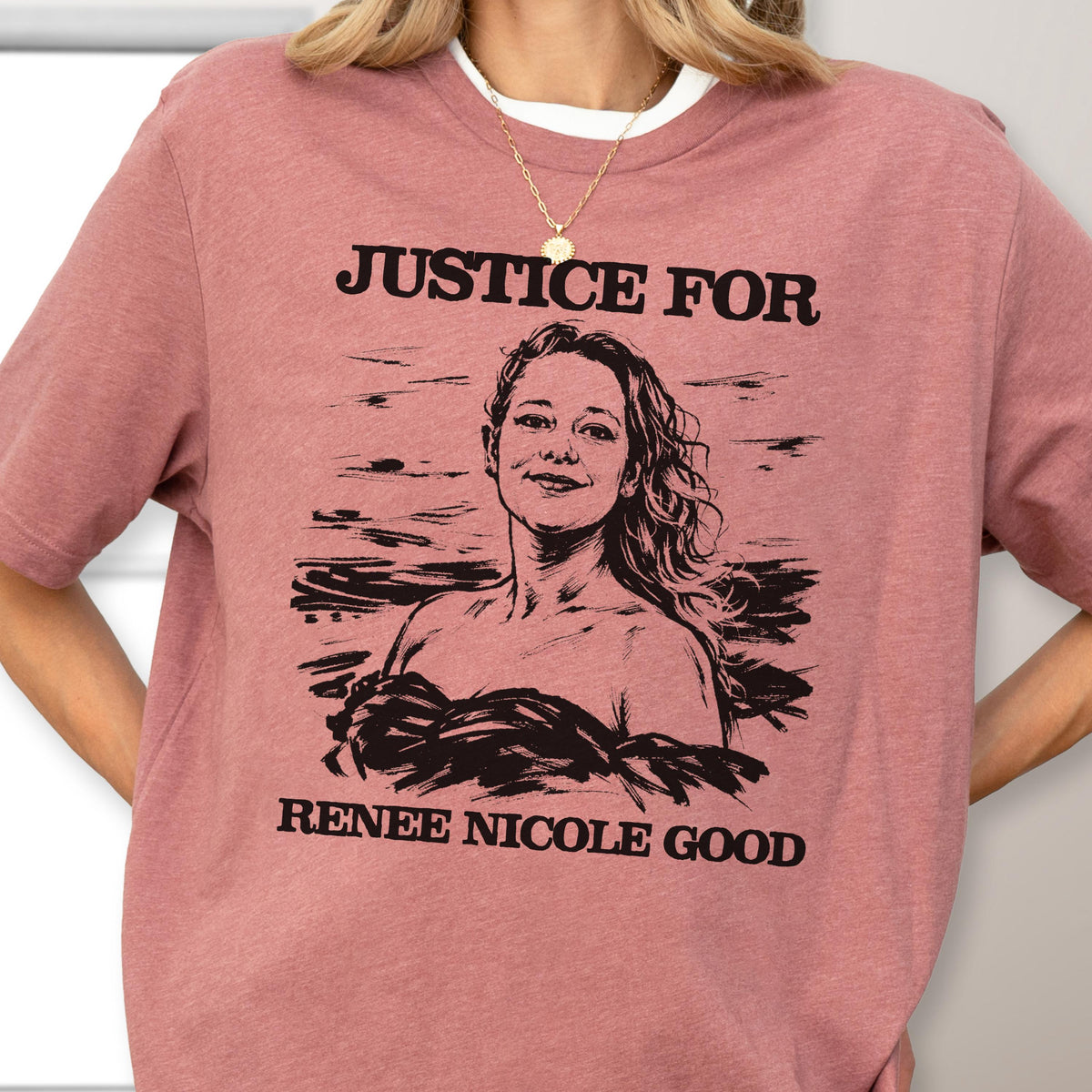 May include: A dusty rose t-shirt with the words "JUSTICE FOR" above a black and white illustration of a woman. Below the illustration, the text reads "RENEE NICOLE GOOD". The shirt has short sleeves.