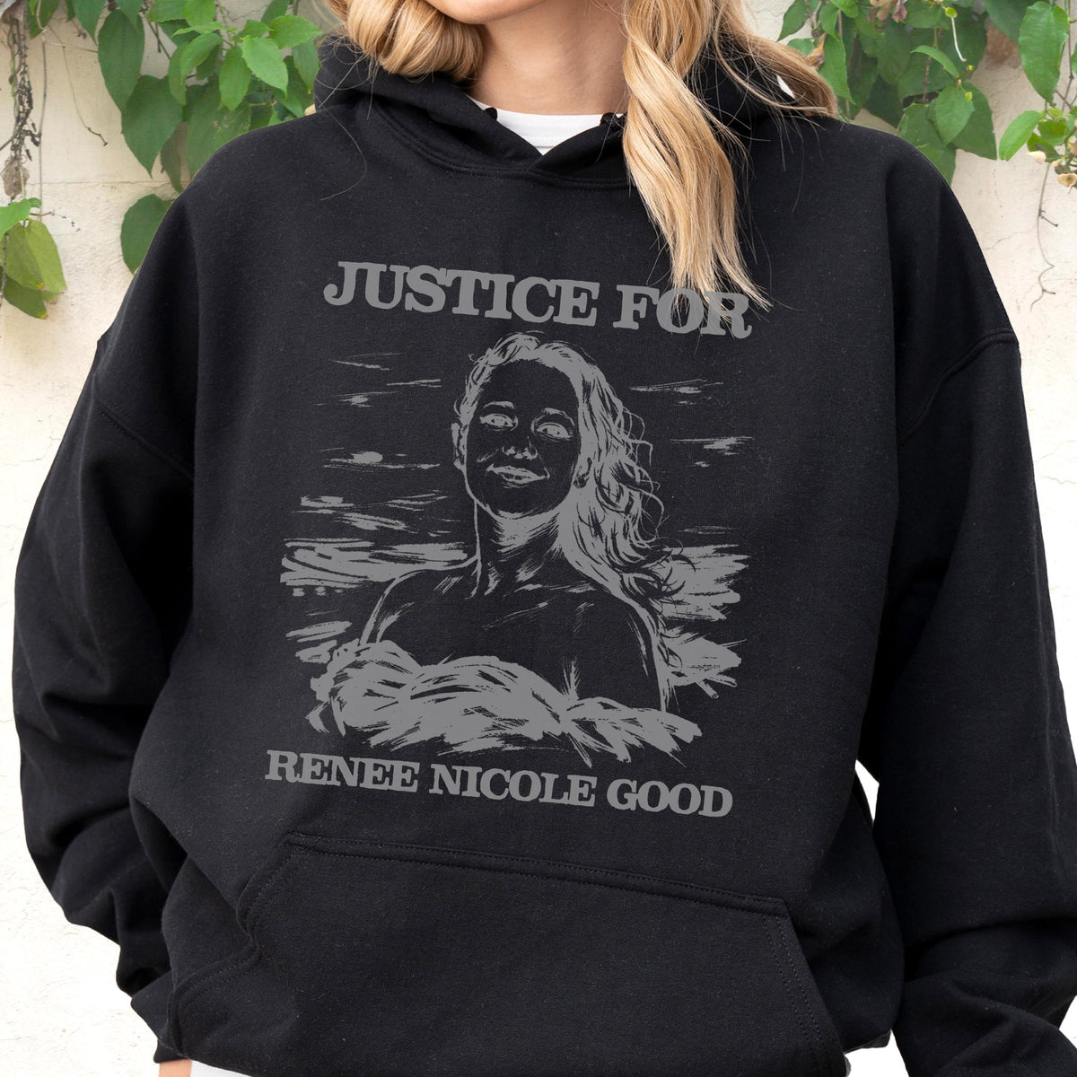 May include: Black hooded sweatshirt with the text "JUSTICE FOR RENEE NICOLE GOOD" in gray. The design features a gray portrait of a woman. The sweatshirt is a casual garment.