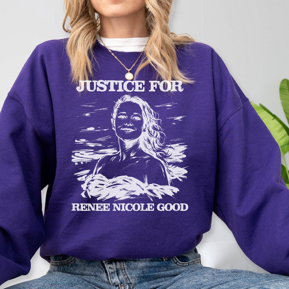 May include: A purple sweatshirt with the text "JUSTICE FOR" above a portrait of a woman and the text "RENEE NICOLE GOOD" below. The graphic is in white. The sweatshirt has long sleeves.