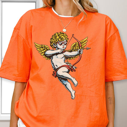 May include: A bright orange t-shirt featuring a graphic print of a cherub with golden wings, curly hair, and red heart-shaped sunglasses. The cherub is depicted in a flying pose, holding a red bow and arrow, rendered in a classic illustrative style.