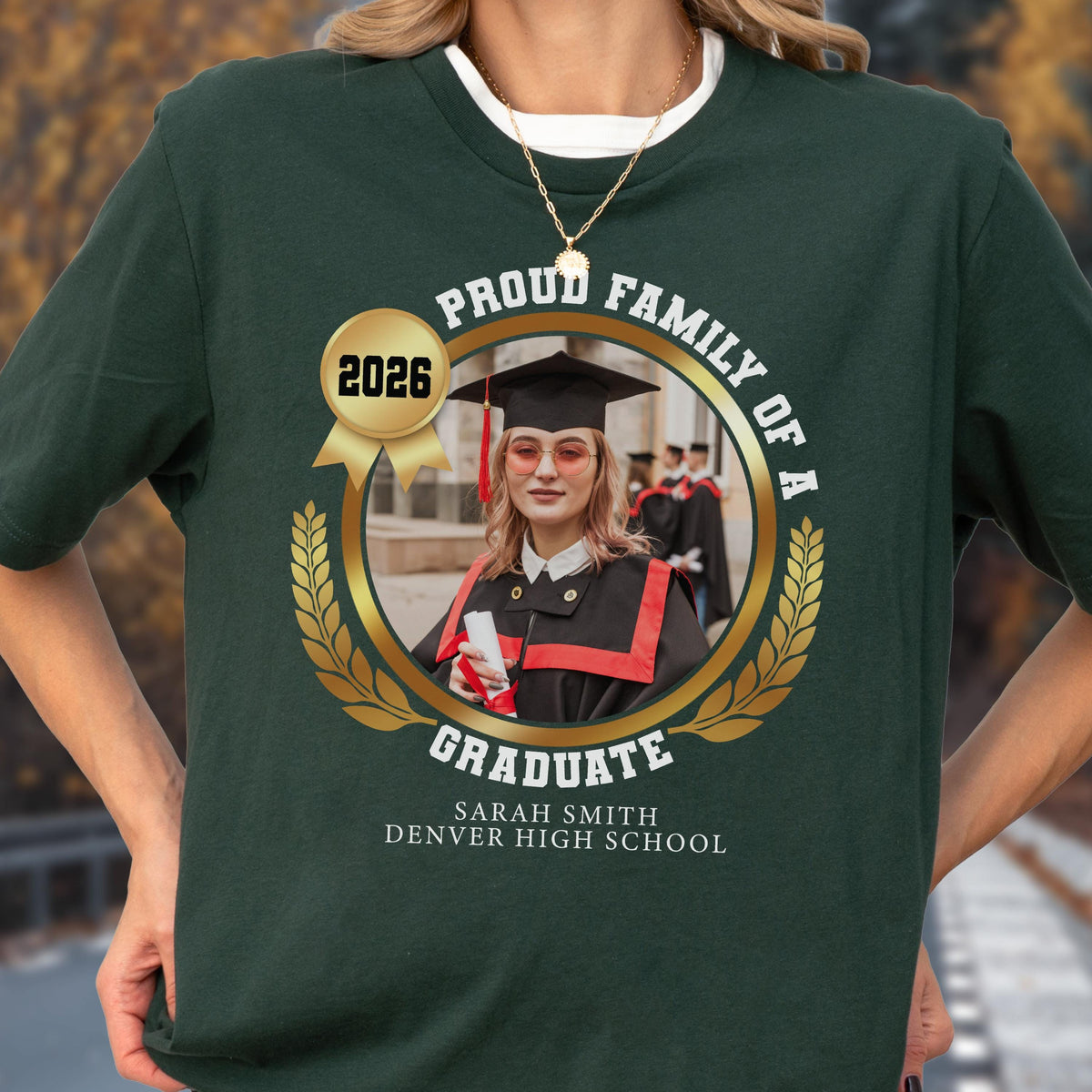 May include: Dark green t-shirt featuring a graduation photo with the text "PROUD FAMILY OF A GRADUATE" and the year "2026". The graduate is wearing a cap and gown. The name "SARAH SMITH" and "DENVER HIGH SCHOOL" are also printed on the shirt.