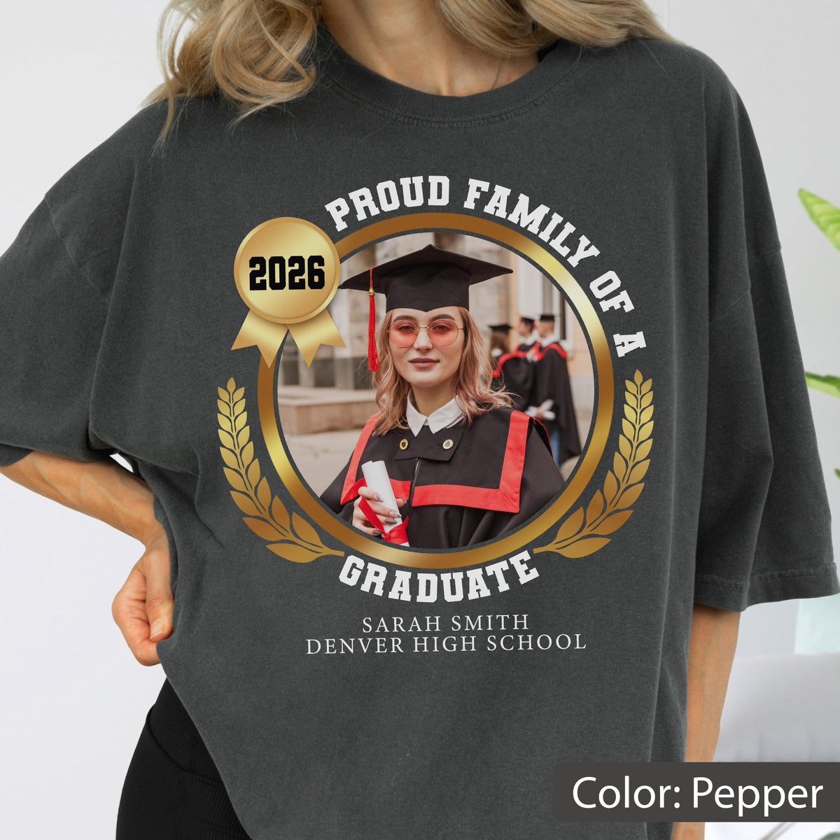 May include: Pepper-colored t-shirt with a graduation design. The design includes a photo of a graduate, the text "Proud Family of a Graduate," the year 2026, and the graduate's name and high school.